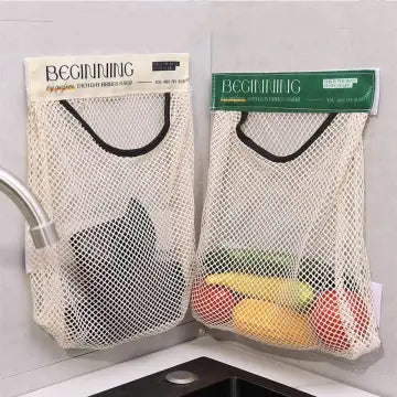 Two mesh produce bags labeled 'Beginning' with fruits and vegetables inside, hanging on a kitchen sink.