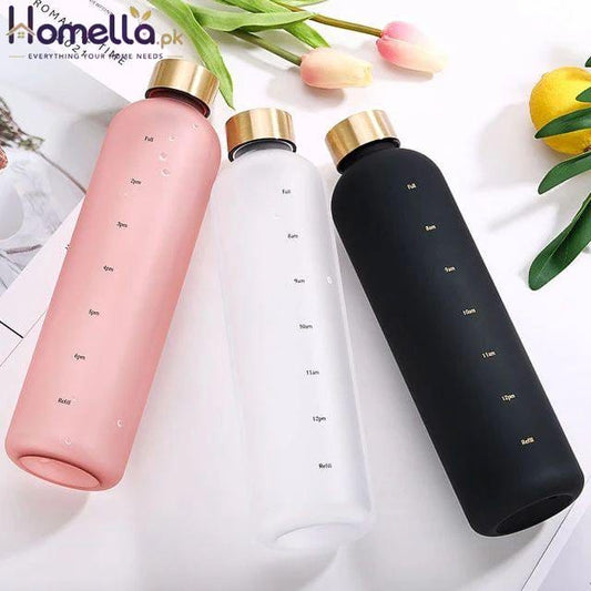 Three water bottles in pink, white, and black with gold caps on a light background.
