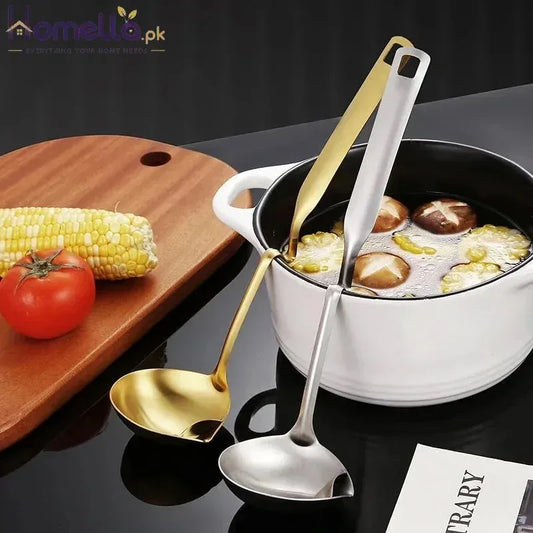 Two spoons, one gold and one silver, in a pot with food on a dark surface with a wooden board and vegetables.