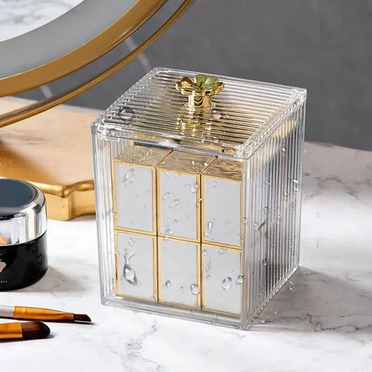 Clear decorative box with gold accents on a marble surface with makeup items.