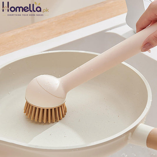 Person using a dishwashing brush on a white frying pan in a kitchen setting