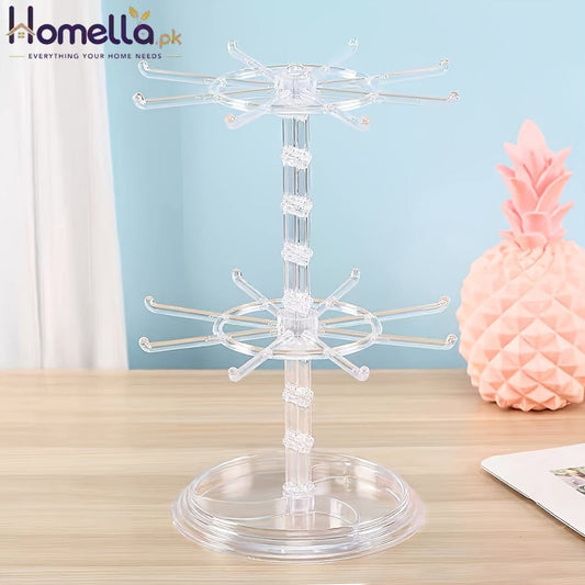 Clear acrylic jewelry display stand on a wooden surface with a pink decorative pineapple in the background.