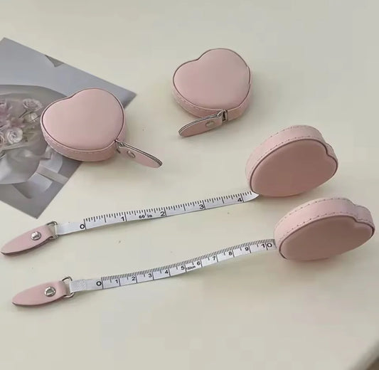 Pink heart-shaped measuring tape with a case on a light surface