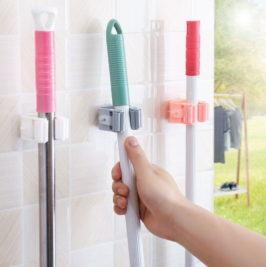 Hand holding a cleaning tool with pink and green attachments against a tiled wall.