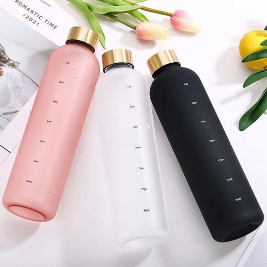 Three water bottles in pink, white, and black with gold caps on a light background.