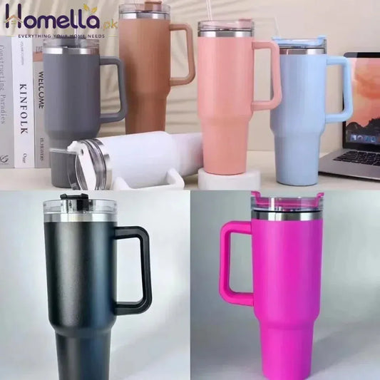 Collection of colorful insulated travel mugs on a desk with books and a laptop.