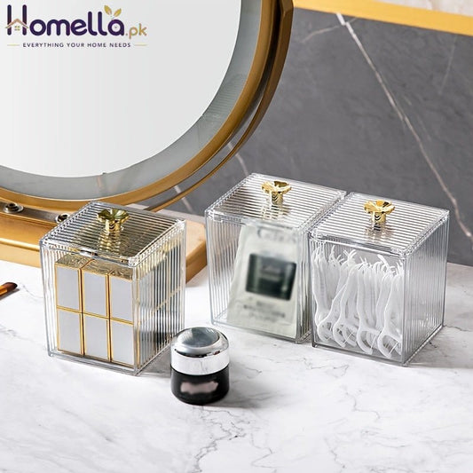 Two clear square containers with gold accents on a marble surface.
