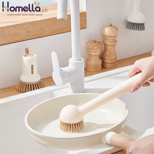 Person using a dishwashing brush in a kitchen sink with wooden utensils on the counter.