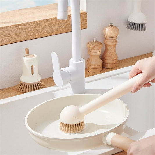 Person using a dishwashing brush in a kitchen sink with wooden utensils on the counter.