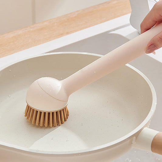 Person using a dishwashing brush on a white frying pan in a kitchen setting