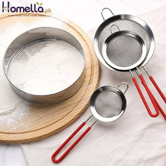 Three metal sifters with red handles on a white surface, one sifting flour.