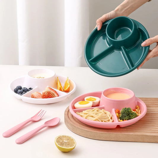 Two divided plates, one green and one pink, with food and cutlery on a white surface.